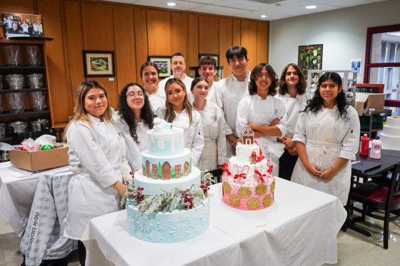 A group of students in chef uniforms, standing around decorated holiday cakes.